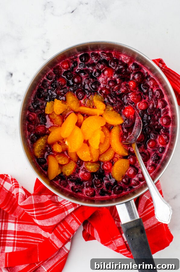 Homemade Cranberry Sauce with Mandarin Oranges 5 Mandarin oranges being added to partially cooked cranberries in a saucepan