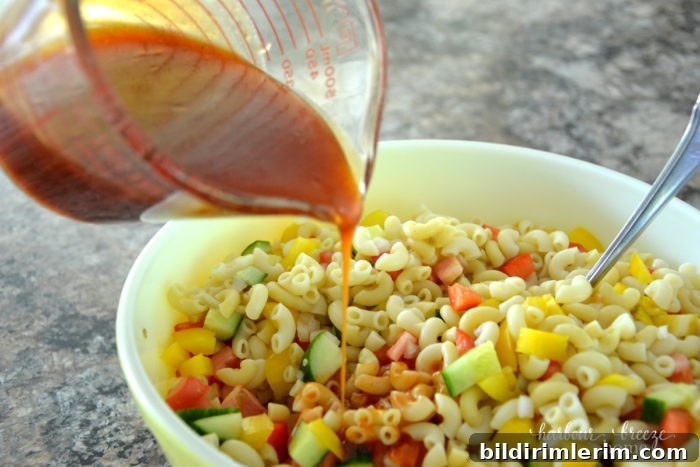 Macaroni Salad with Tangy Ketchup Dressing 7 ketchup dressing being poured on a bowl of cold pasta salad.