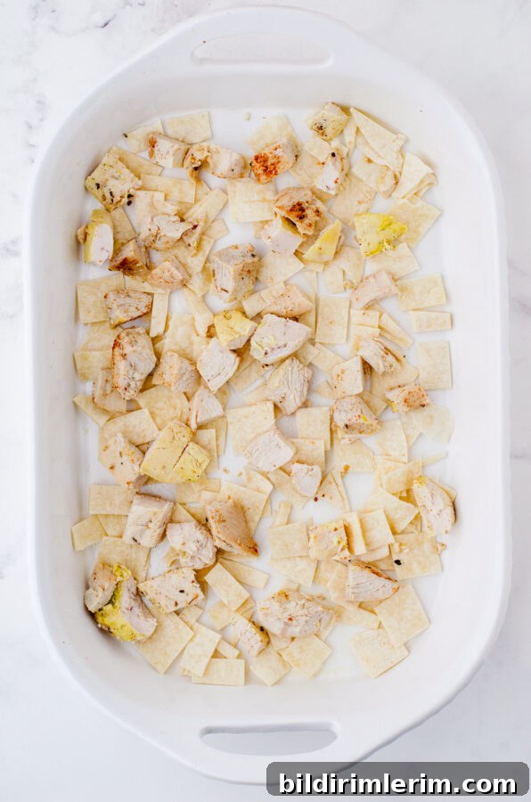 Cheesy One-Pan Mexican Chicken Casserole 6 Diced cooked chicken layered over cut up flour tortillas in a baking dish for Mexican Chicken Casserole